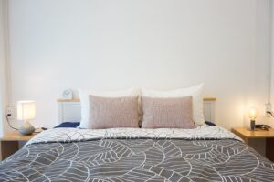 A perfectly made bed with patterned duvet cover and two bedside lamps giving a warm glow to the beige room