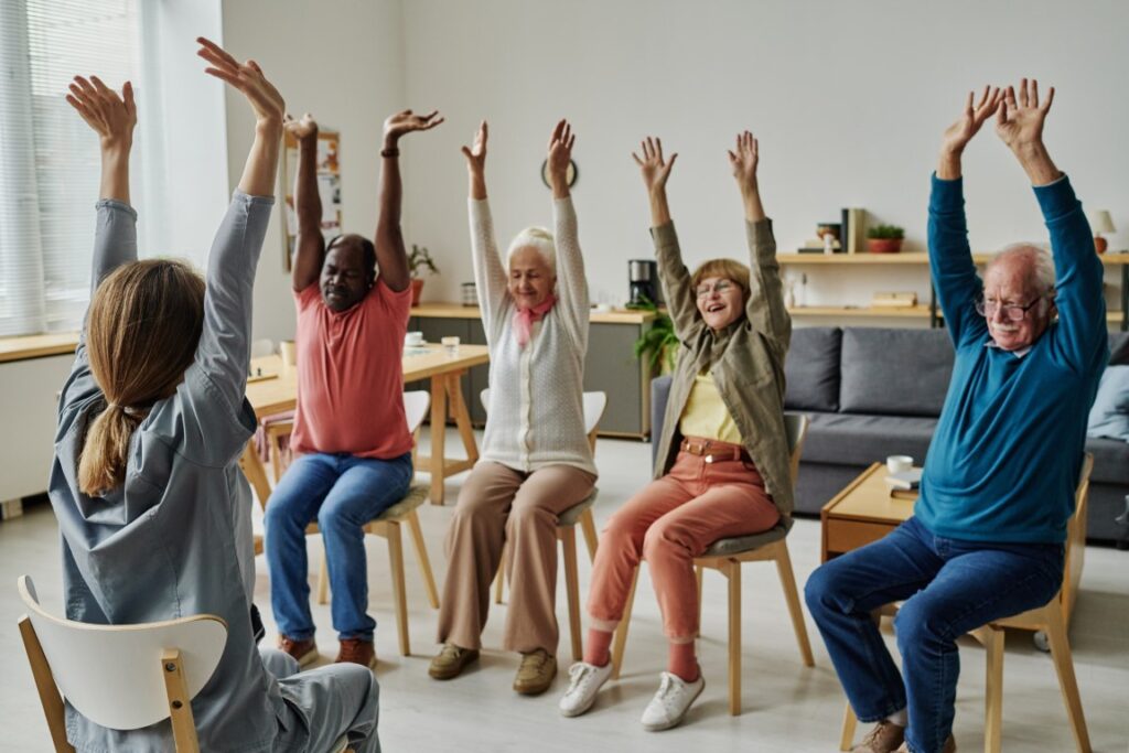 Group of senior people sitting on chairs and doing yoga with the instructor at a retirement community