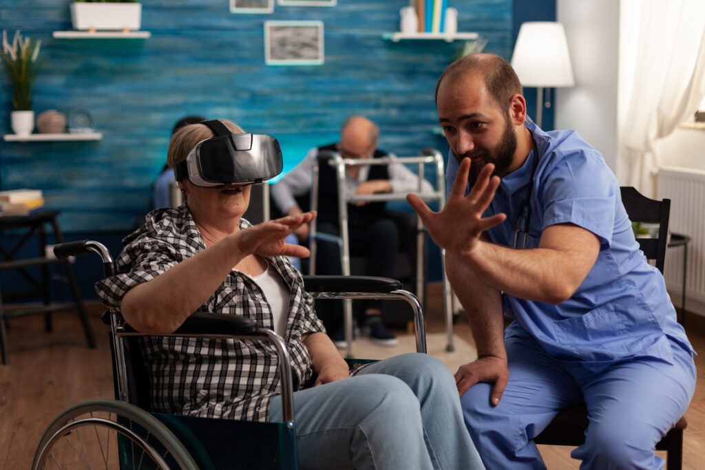 Male nurse teaching an elderly woman how to use virtual reality goggles in senior home