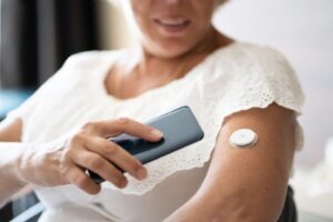 Older woman tapping her smartphone on a continuous health monitoring devices to measure glucose levels