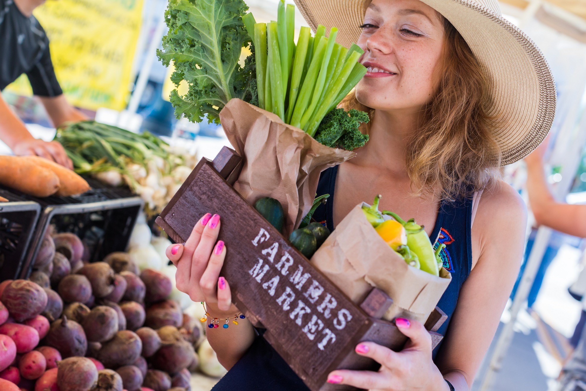 Young lady smiling and holding a box of produce at a farmers market