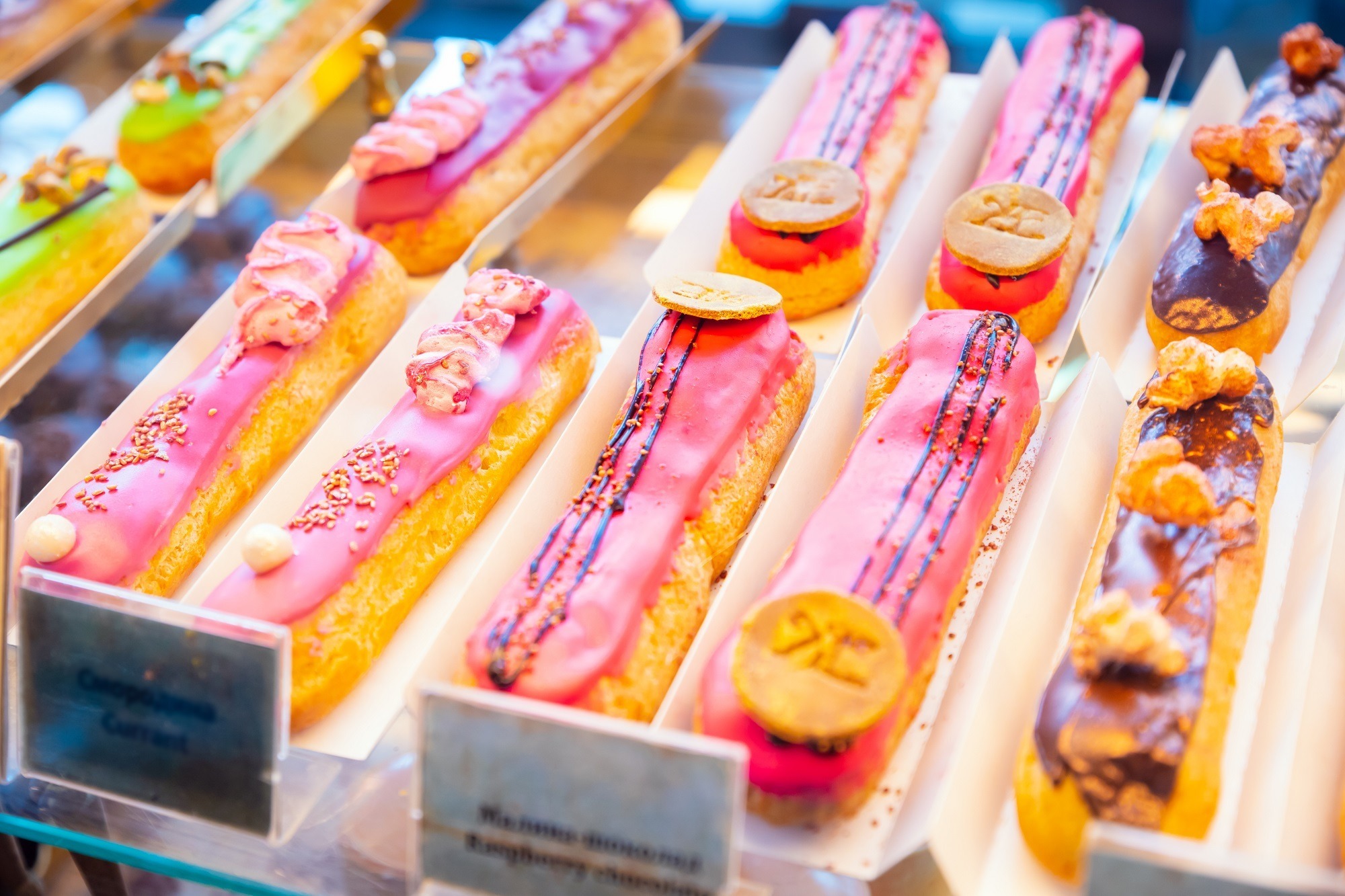 Rows of eclairs with colourful ganache sitting on a shelf