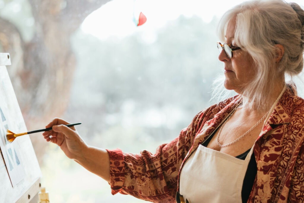 Older lady standing at an easel painting watercolours on paper