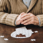 Cropped view of a senior man sitting with an incomplete head-shaped puzzle in front of him