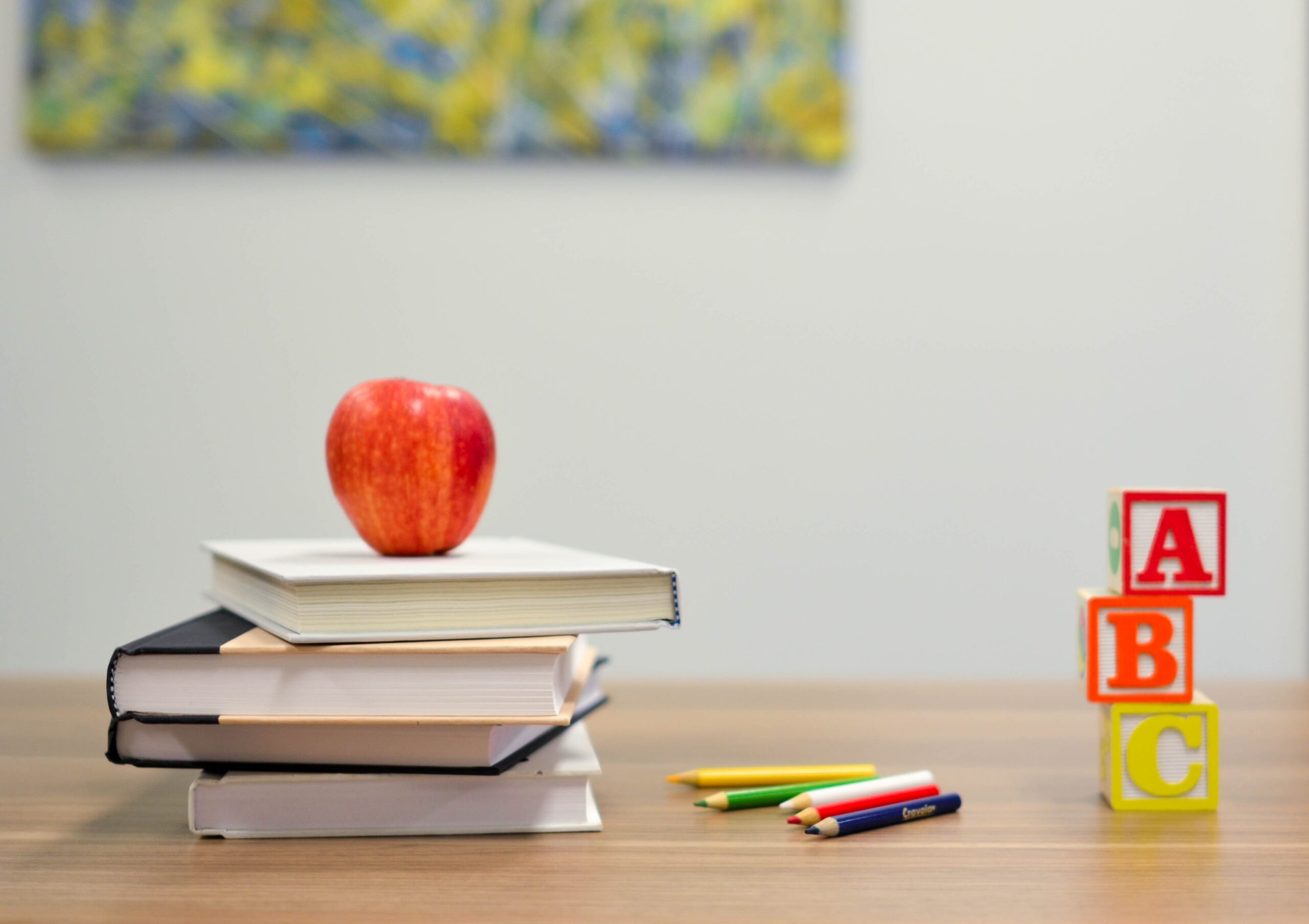 A table holding a stack of books with an apple on top, some colour pencils, and ABC blocks