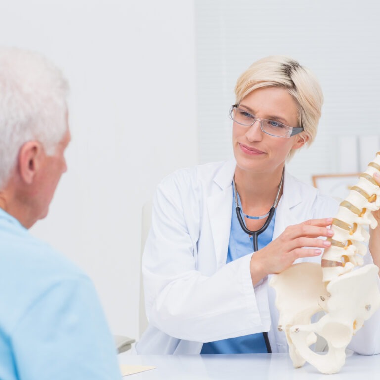 Older patient in a doctor's office discussing back issues on a skeleton