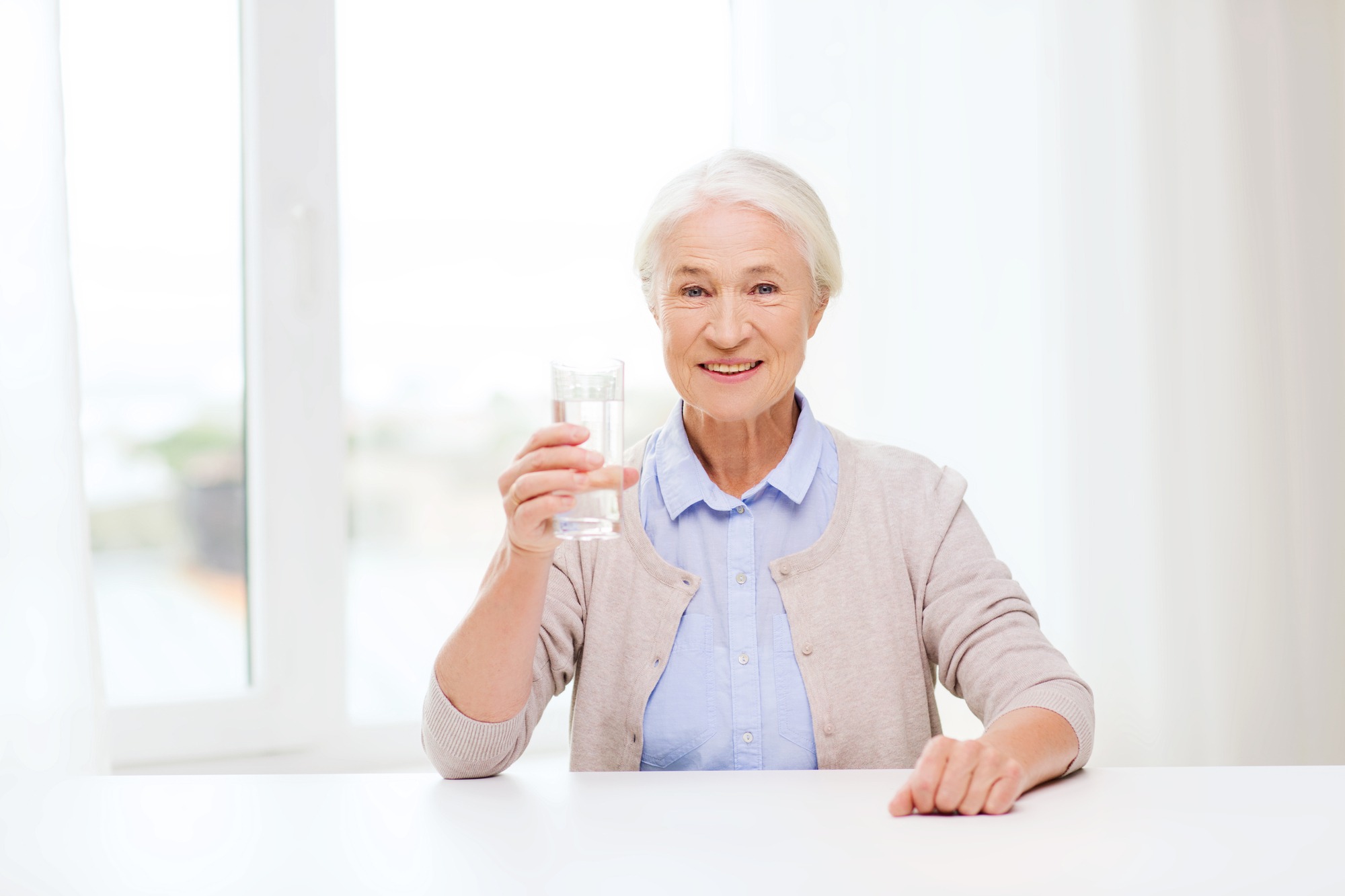 Happy senior woman with a glass of water at home