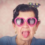 Senior woman in a good mood wearing funky heart-shaped glass and sticking her tongue out