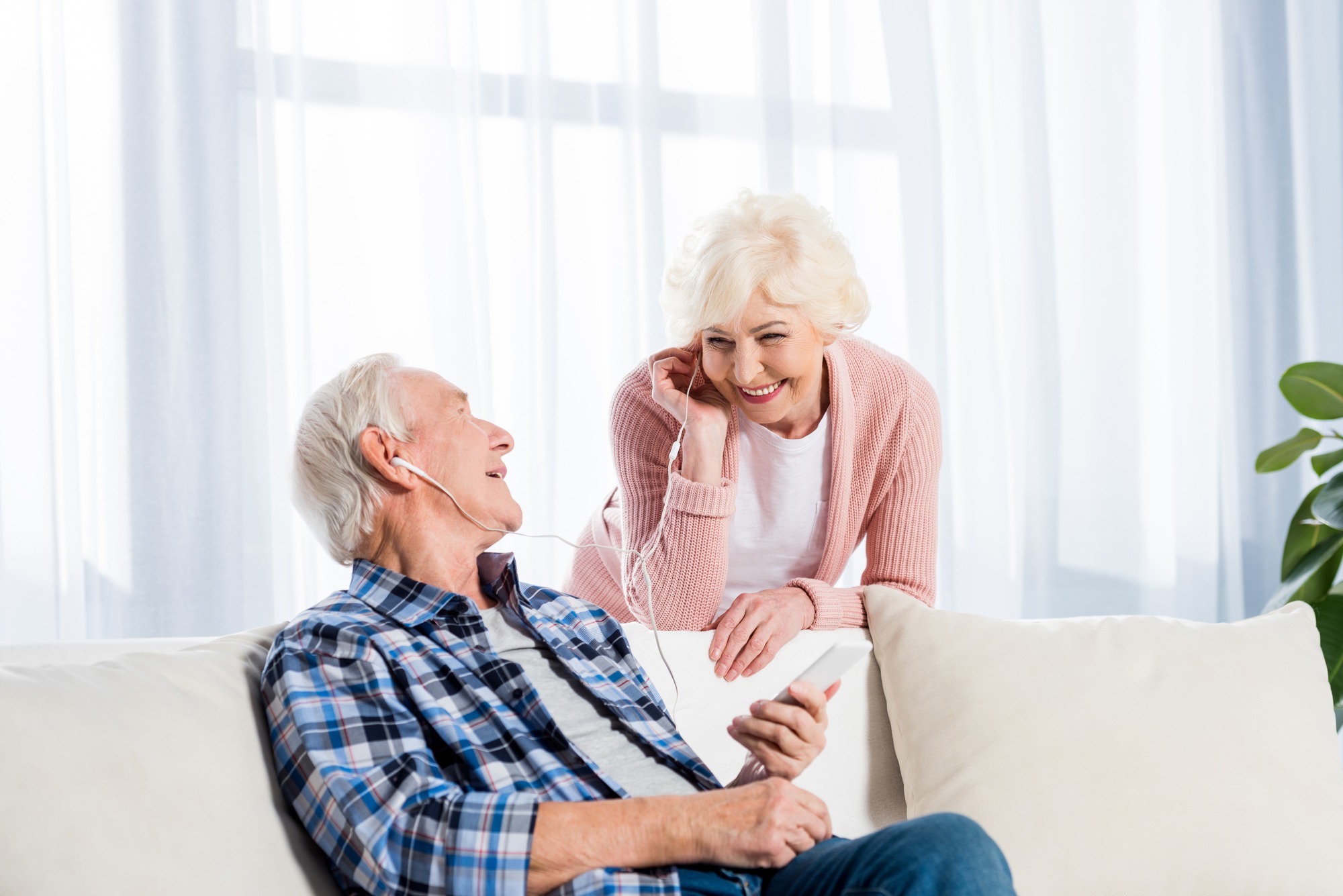 Happy senior couple in earphones listening to music together at home