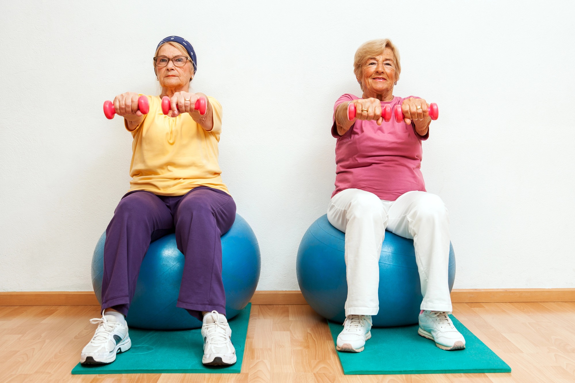 Two elderly women doing muscle exercises with weights in the gym