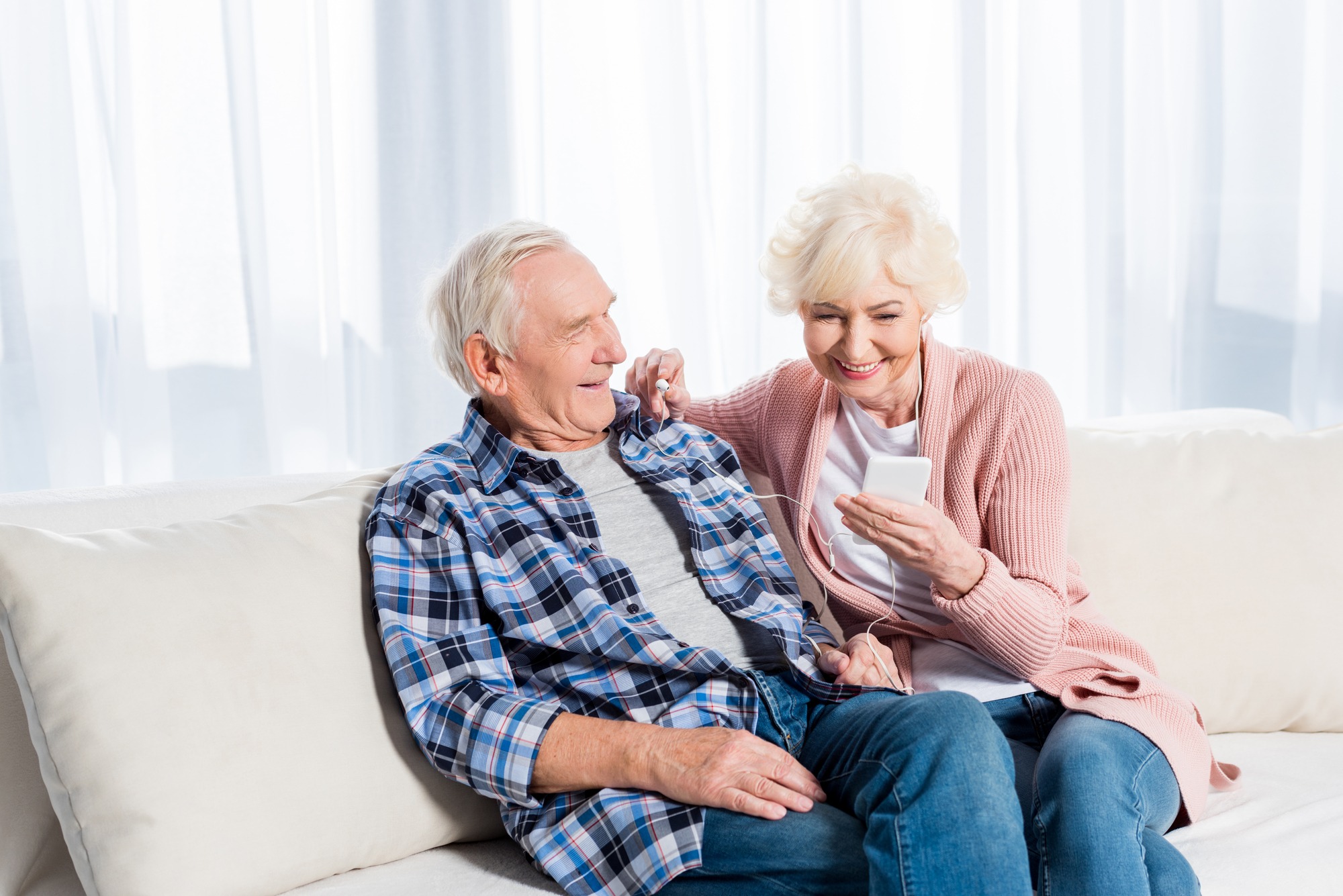 Happy senior couple in earphones listening to music together at home