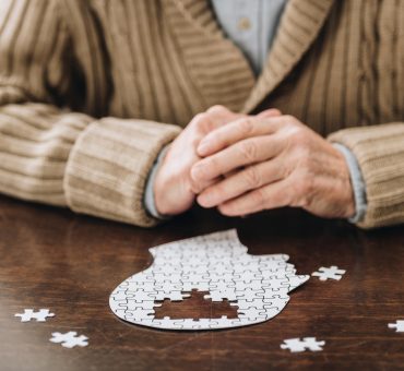 Cropped view of a senior man sitting with an incomplete head-shaped puzzle in front of him