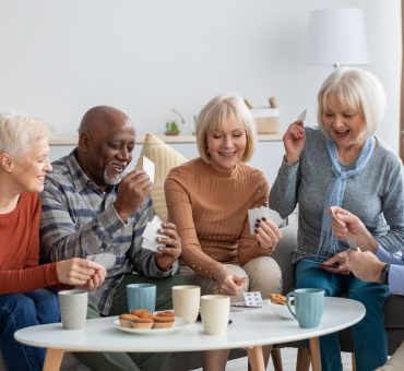 Happy group of seniors having tea and playing a card game at home