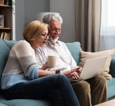 Elderly retired couple sitting at home surfing the internet on a laptop