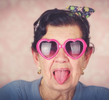 Senior woman in a good mood wearing funky heart-shaped glass and sticking her tongue out