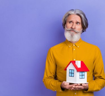 Senior man looking thoughtful while holding a toy model of senior apartments