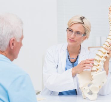 Older patient in a doctor's office discussing back issues on a skeleton