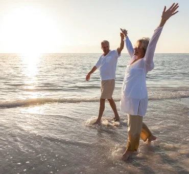 Happy senior retirees holding hands and walking along the beach