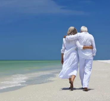 Senior couple walking along a white sandy beach in their retirement