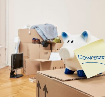 Packed moving boxes with a piggy bank on top and a post-it note on it saying “Downsizing”