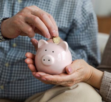 A senior man drops a coin into a ceramic piggy bank held by his wife