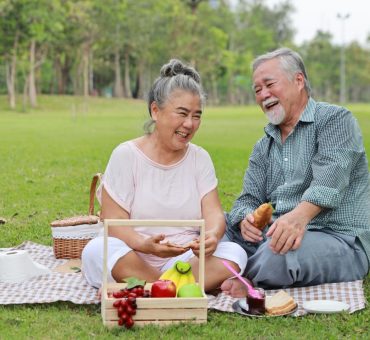 Laughing Asian senior couple sitting on a blanket and having a picnic together in Coquitlam parks