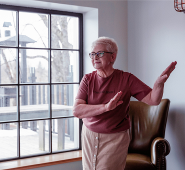 Senior lady dancing in her light-filled sitting room with a large window overlooking the backyard