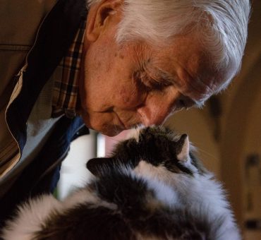 Old man nose-booping a fluffy black and white cat