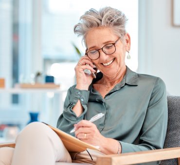 Smiling older lady talking on the phone while taking notes about senior residence options