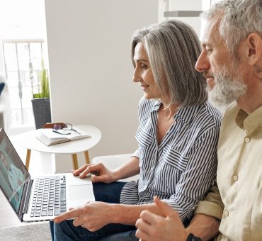Senior couple having an online telemedicine consultation with a virtual doctor in BC using their laptop computer as they sit on their couch at home
